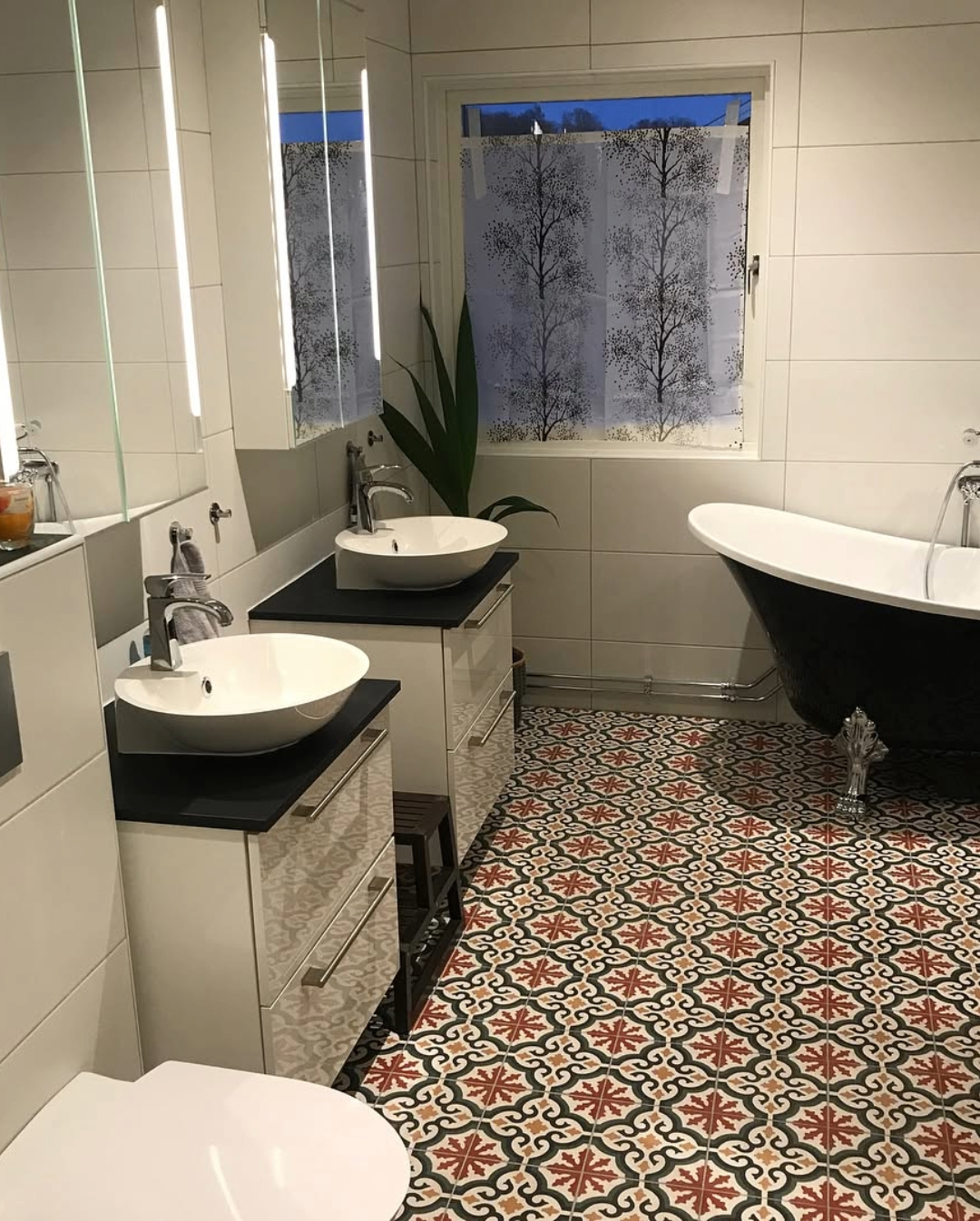 badrum med två fristående handfat, svart badkar med tassar och färgglatt klinkergolv